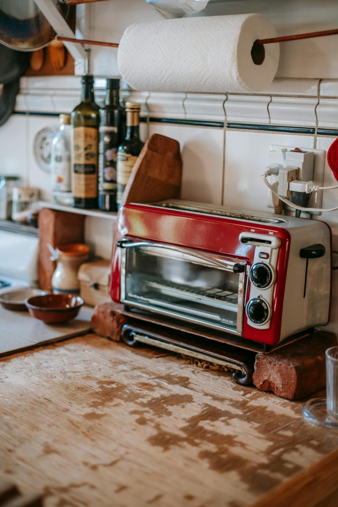 This image depicts a retro-look and warm kitchen counter with a red-themed toaster oven, olive oil, a paper-towel holder and a tile back-splash with a worn butcher-block counter top